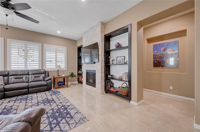 tiled living room with a stone fireplace, built in features, and ceiling fan