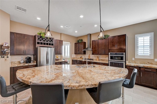 kitchen with a kitchen island with sink, wall chimney range hood, stainless steel appliances, and a kitchen breakfast bar