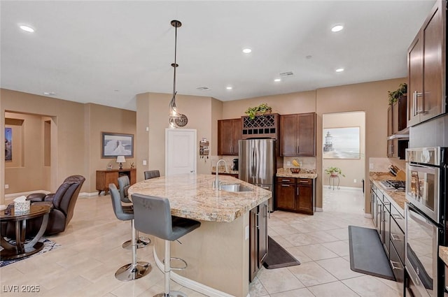 kitchen with decorative light fixtures, sink, a breakfast bar area, light stone counters, and a center island with sink