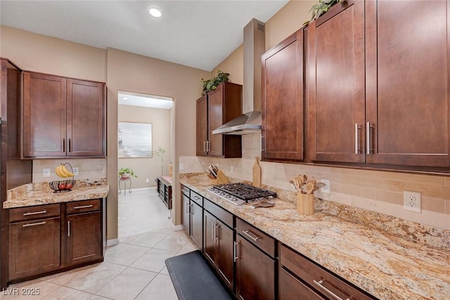 kitchen with tasteful backsplash, wall chimney range hood, light stone countertops, and stainless steel gas stovetop