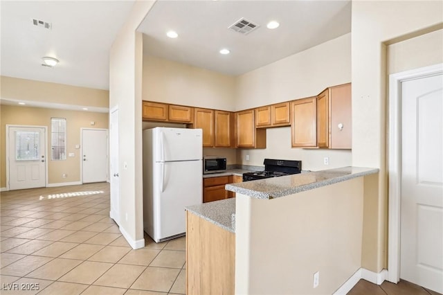 kitchen featuring light tile patterned floors, white refrigerator, black range with gas stovetop, kitchen peninsula, and light stone countertops