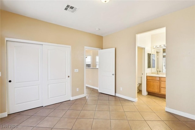 unfurnished bedroom featuring sink, light tile patterned floors, ensuite bath, and a closet