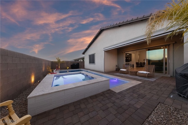 pool at dusk with a patio and an in ground hot tub