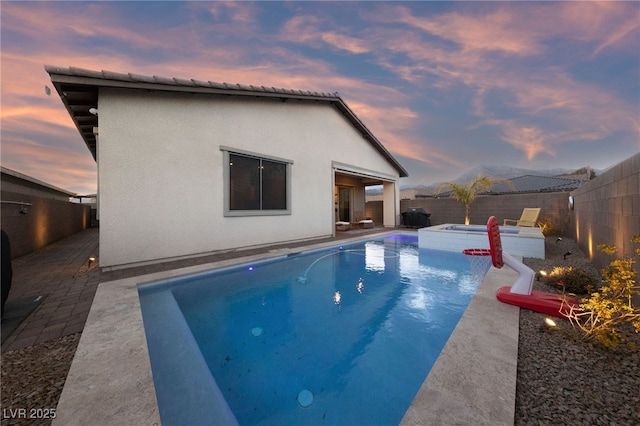 pool at dusk featuring an in ground hot tub and a patio