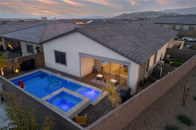 pool at dusk featuring an in ground hot tub, a mountain view, and central AC