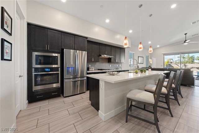 kitchen featuring a breakfast bar, sink, decorative light fixtures, appliances with stainless steel finishes, and an island with sink