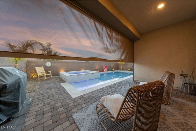 pool at dusk featuring an in ground hot tub, area for grilling, and a patio area