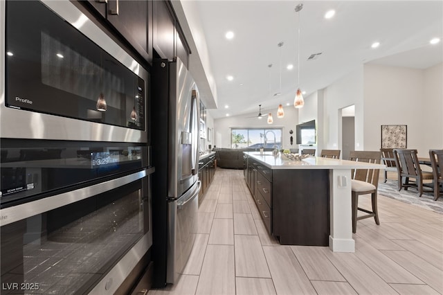 kitchen featuring vaulted ceiling, an island with sink, a kitchen breakfast bar, hanging light fixtures, and stainless steel appliances