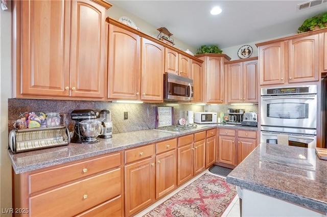 kitchen with appliances with stainless steel finishes, dark stone counters, visible vents, and tasteful backsplash