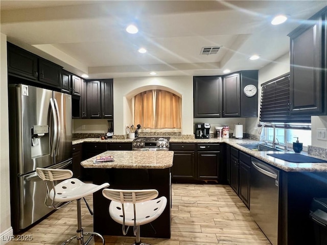 kitchen featuring a kitchen island, a raised ceiling, sink, stainless steel appliances, and light hardwood / wood-style flooring