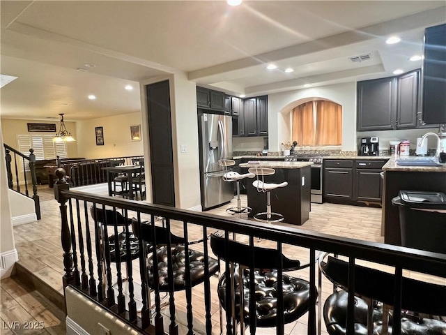 kitchen with a kitchen island, appliances with stainless steel finishes, sink, light stone countertops, and light wood-type flooring