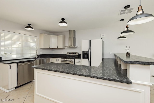 kitchen with appliances with stainless steel finishes, pendant lighting, white cabinetry, sink, and wall chimney range hood