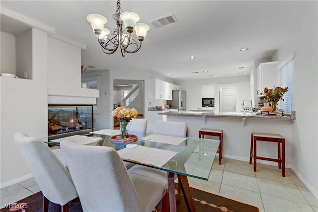 dining space featuring a multi sided fireplace, sink, light tile patterned floors, and an inviting chandelier