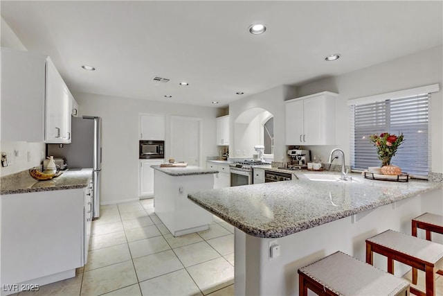 kitchen featuring a breakfast bar area, appliances with stainless steel finishes, light stone countertops, white cabinets, and kitchen peninsula