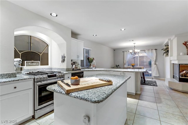 kitchen with a multi sided fireplace, a kitchen island, white cabinets, gas stove, and light stone countertops