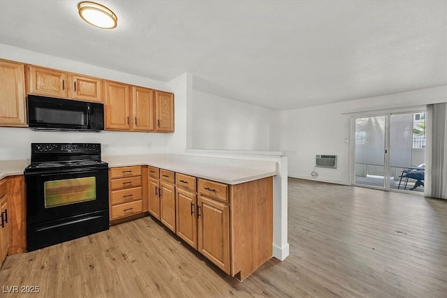 kitchen with light hardwood / wood-style flooring, kitchen peninsula, a wall unit AC, and black appliances