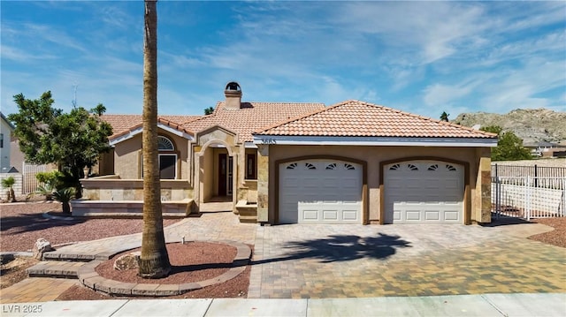 mediterranean / spanish-style home featuring fence, a tiled roof, stucco siding, a chimney, and decorative driveway