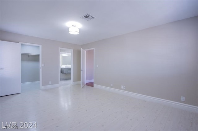 unfurnished bedroom with a closet, a walk in closet, ensuite bath, and light hardwood / wood-style flooring