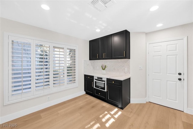 kitchen with light stone countertops, oven, decorative backsplash, and light wood-type flooring