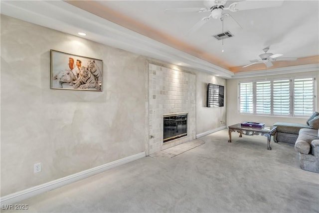 carpeted living room featuring a tile fireplace, a raised ceiling, and ceiling fan