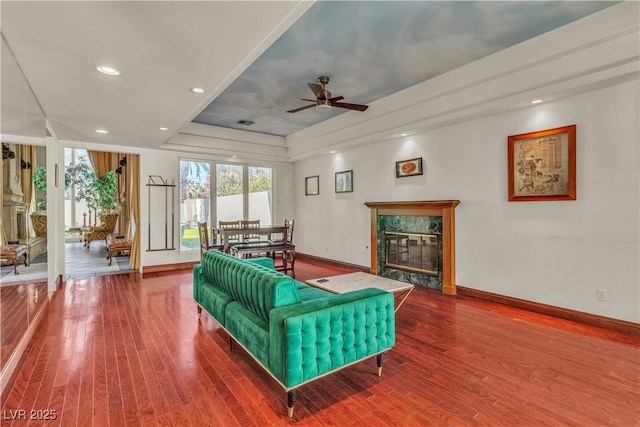 living room featuring ceiling fan, wood-type flooring, a fireplace, and a raised ceiling