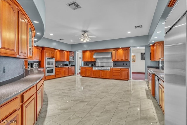 kitchen featuring tasteful backsplash, ceiling fan, wall chimney exhaust hood, and appliances with stainless steel finishes