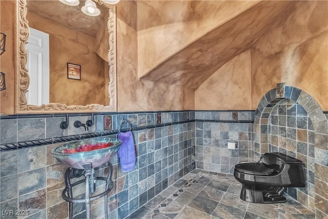 bathroom with toilet, sink, and tile walls