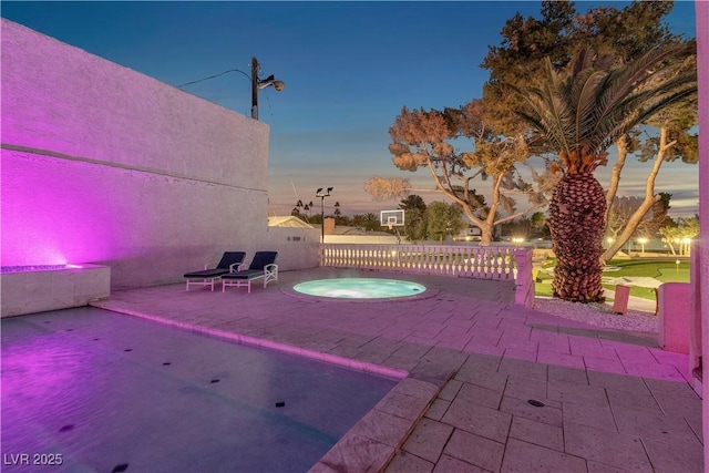 pool at dusk with an in ground hot tub and a patio area