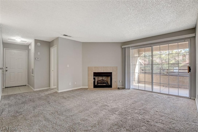 unfurnished living room with light carpet, a tiled fireplace, and a textured ceiling