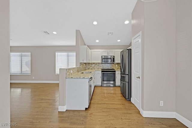 kitchen with sink, appliances with stainless steel finishes, light stone counters, tasteful backsplash, and white cabinets