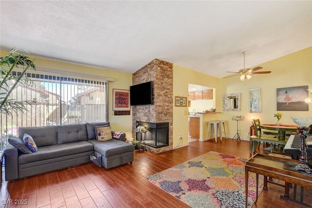 living room with vaulted ceiling, a fireplace, hardwood / wood-style flooring, ceiling fan, and a textured ceiling