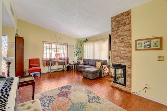 living room featuring lofted ceiling, wood-type flooring, a stone fireplace, and a textured ceiling