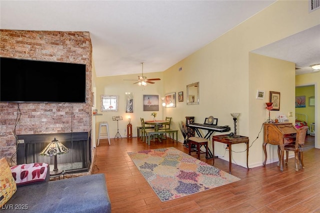 living room featuring lofted ceiling, a brick fireplace, hardwood / wood-style flooring, and ceiling fan