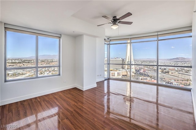 empty room featuring wood-type flooring, ceiling fan, and a wall of windows