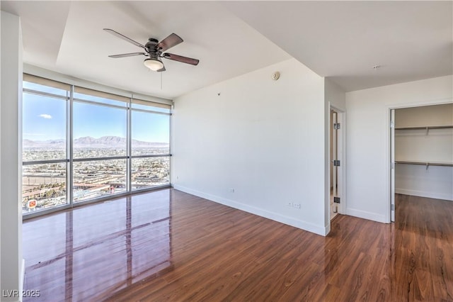 empty room featuring expansive windows, ceiling fan, dark hardwood / wood-style floors, and a mountain view