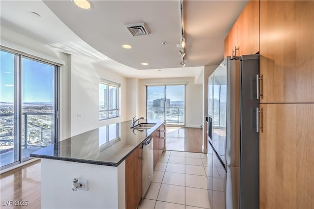 kitchen featuring sink, refrigerator with ice dispenser, stainless steel dishwasher, light tile patterned floors, and a center island with sink