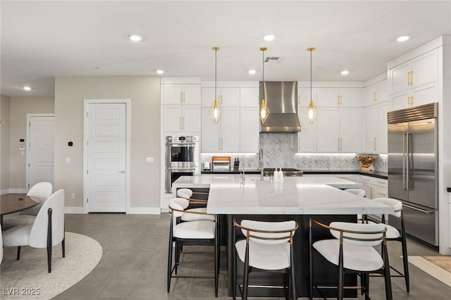 kitchen featuring stainless steel appliances, wall chimney range hood, white cabinets, and decorative light fixtures