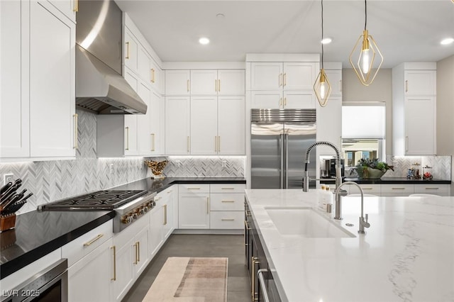 kitchen with dark stone countertops, wall chimney range hood, white cabinets, and appliances with stainless steel finishes