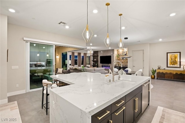 kitchen with light stone counters, sink, decorative light fixtures, and a center island with sink