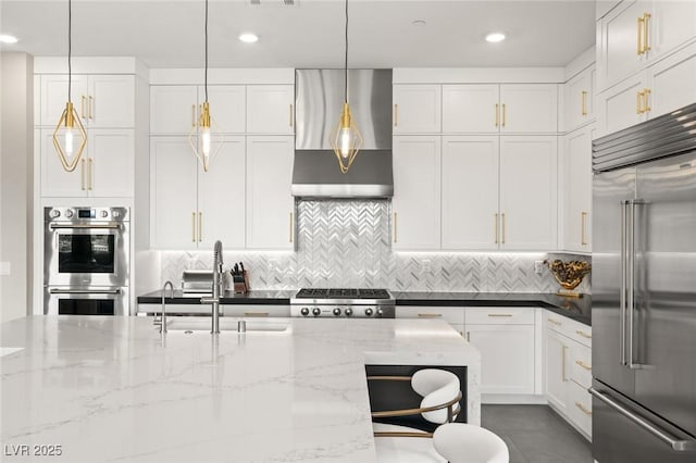 kitchen featuring hanging light fixtures, appliances with stainless steel finishes, white cabinets, and wall chimney exhaust hood