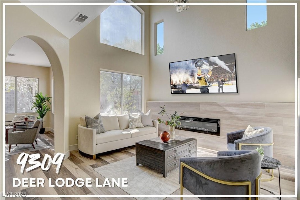 living room with a high end fireplace, plenty of natural light, a high ceiling, and light wood-type flooring