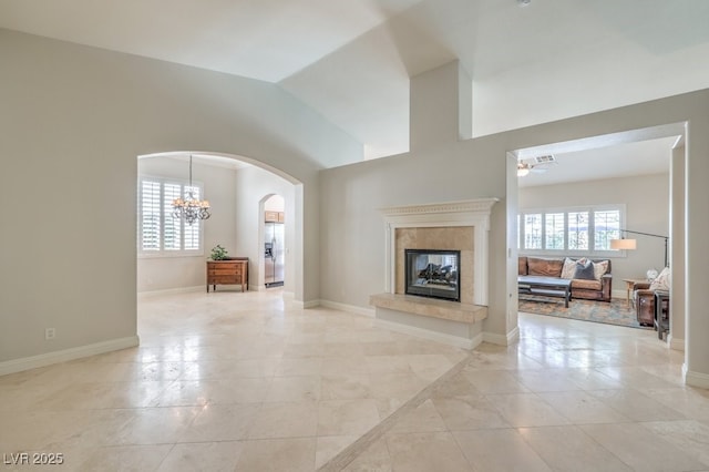 tiled living room with a premium fireplace, vaulted ceiling, a healthy amount of sunlight, and ceiling fan with notable chandelier