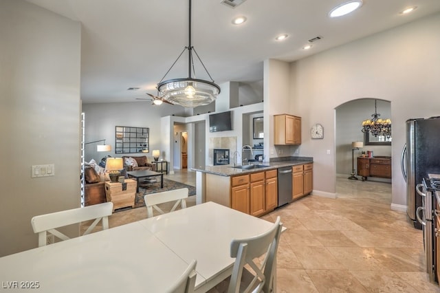 kitchen with sink, hanging light fixtures, stainless steel appliances, a tiled fireplace, and ceiling fan with notable chandelier