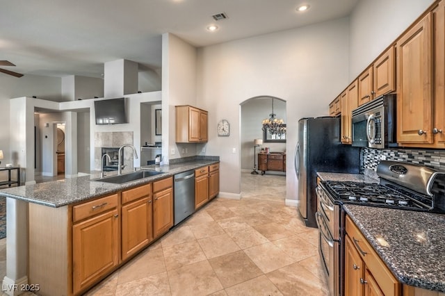 kitchen featuring sink, stainless steel appliances, decorative backsplash, ceiling fan with notable chandelier, and dark stone counters