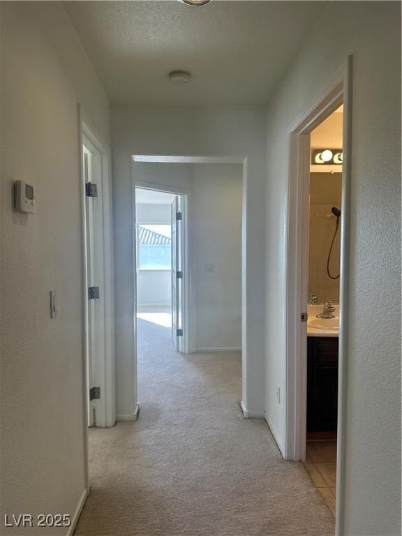 corridor with sink, light carpet, and a textured ceiling