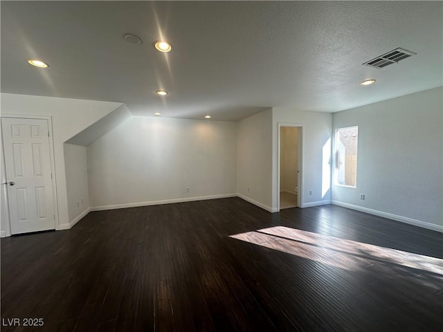 additional living space featuring a textured ceiling and dark hardwood / wood-style flooring