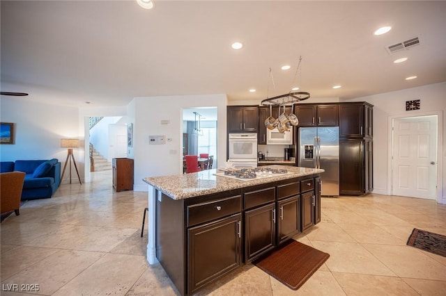 kitchen featuring light stone counters, a center island, dark brown cabinets, a kitchen breakfast bar, and white appliances