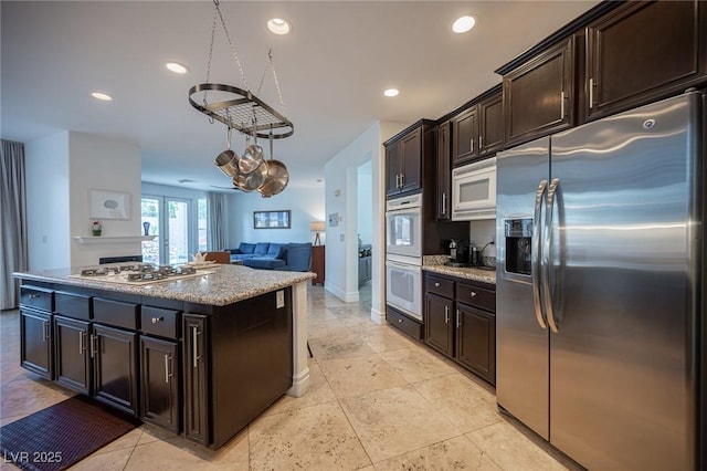 kitchen featuring light stone countertops, a center island, dark brown cabinets, and white appliances