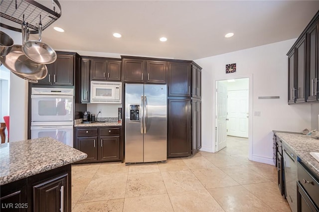 kitchen featuring light tile patterned flooring, dark brown cabinets, light stone counters, and white appliances