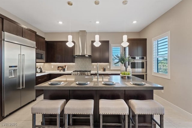 kitchen featuring sink, hanging light fixtures, built in appliances, dark brown cabinetry, and wall chimney range hood